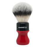 A synthetic shaving brush with a black and red handle, displaying the bristles which are primarily white.