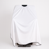 White salon cape draped over a black chair on a white background