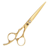 A pair of gold-colored hairdressing scissors with a dragon handle design and a large blue gemstone on the ring.