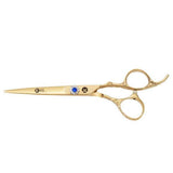 A pair of gold-colored hairdressing scissors with a dragon handle design and a large blue gemstone on the ring.