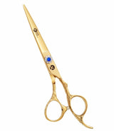 A pair of gold-colored hairdressing scissors with a dragon handle design and a large blue gemstone on the ring.